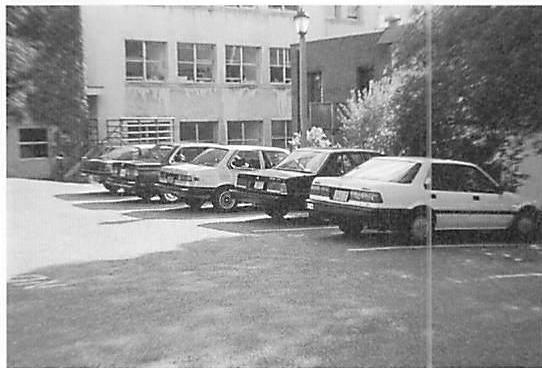 Parking lot with slightly less life. Because the cars are in a uniform row, the space is larger, more homogeneous, less personal.